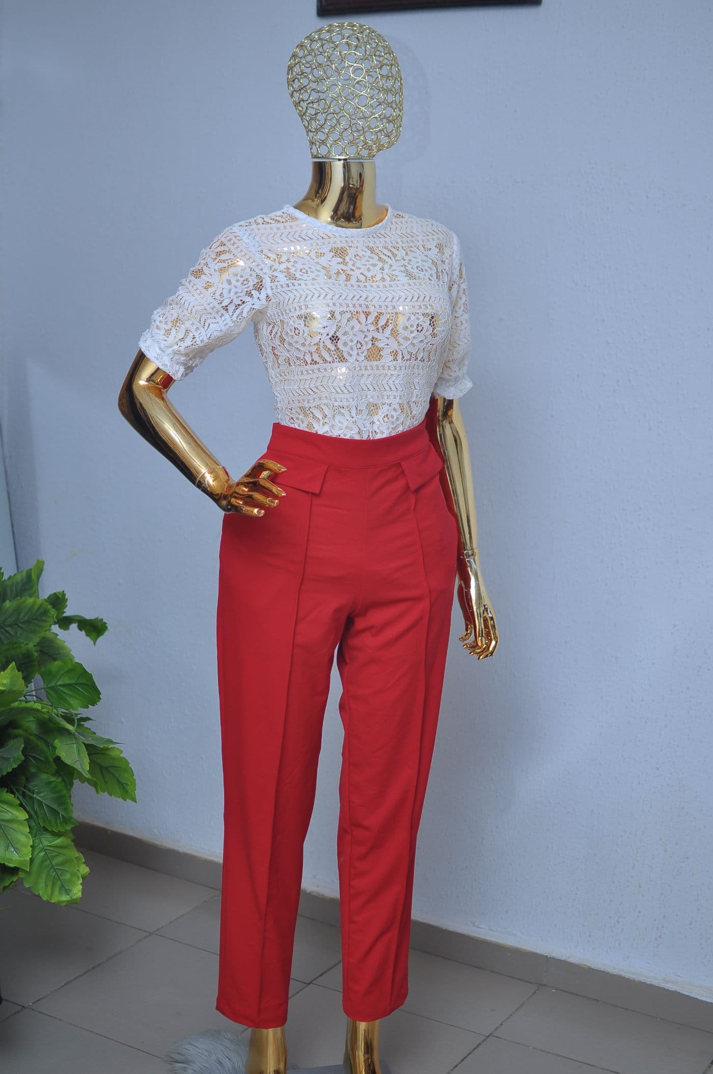 Beaded white lace top with short sleeves, worn with high-waisted red trousers, on a gold mannequin.