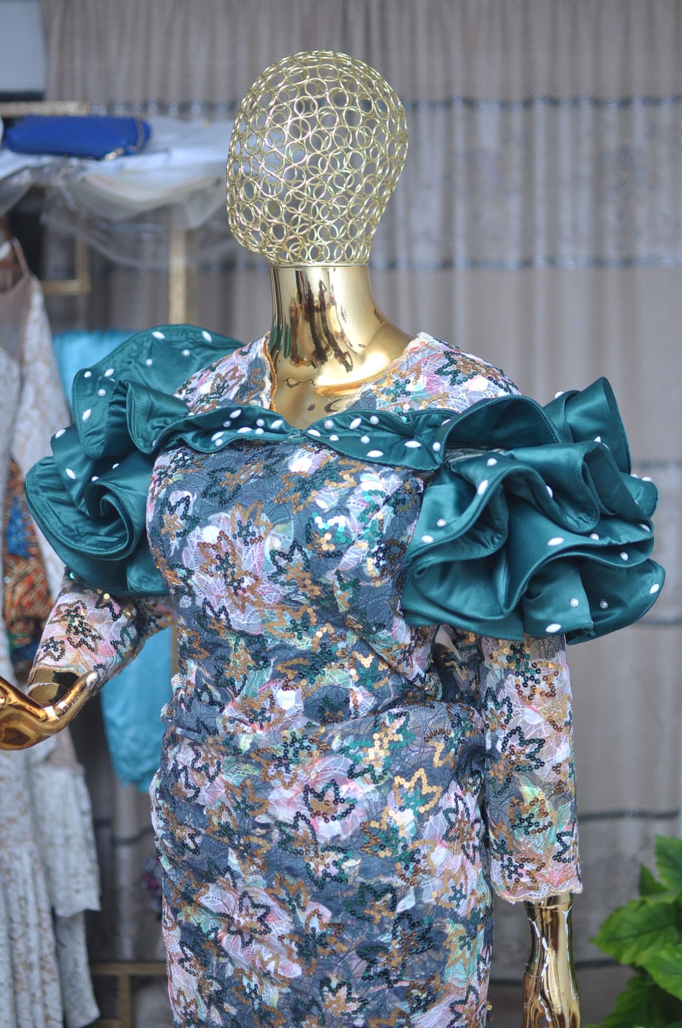 Emerald sequin lace dress with tiered satin shoulders trimmed with pearls, on a gold mesh mannequin.