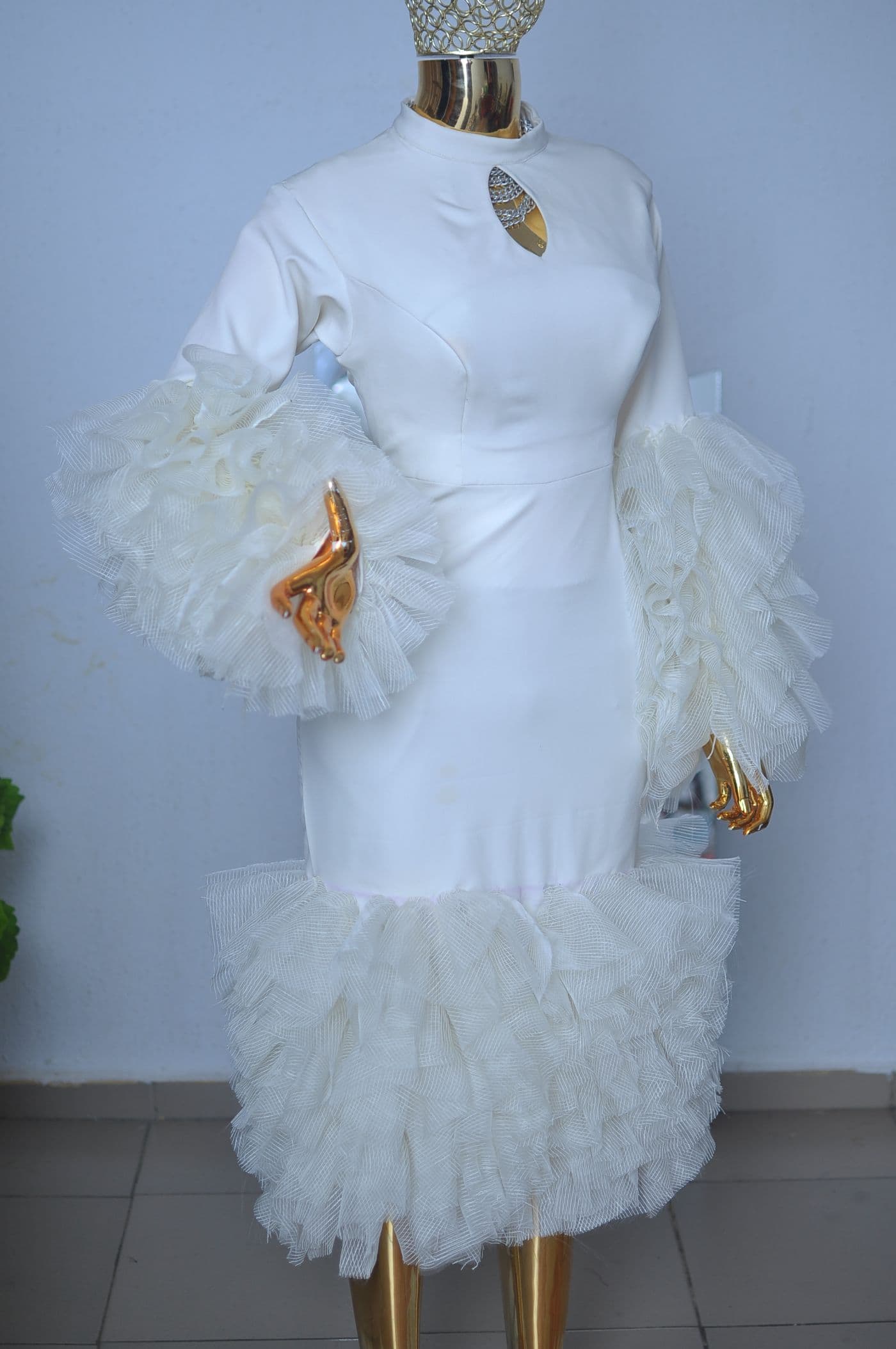 Ivory fitted dress with layered tulle ruffle sleeves and hem, on a gold mannequin.