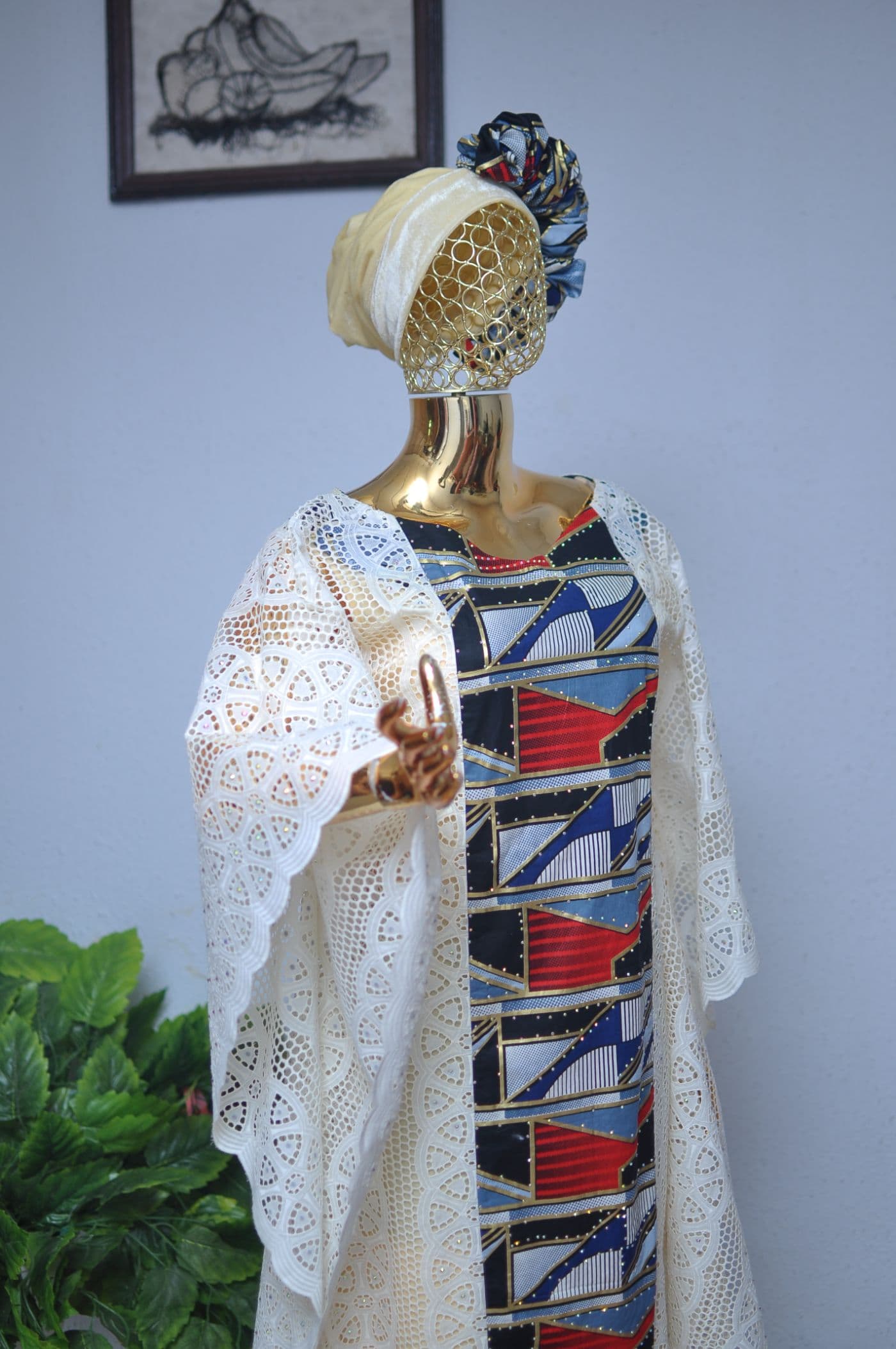 Cream eyelet lace layered over an Ankara panel, with a matching head wrap, on a gold mannequin.