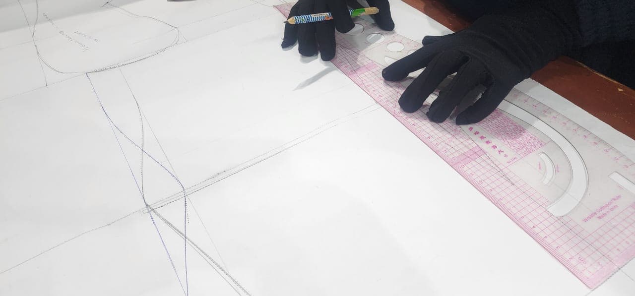 Hands marking a pattern with a curve ruler and pencil, no face shown.
